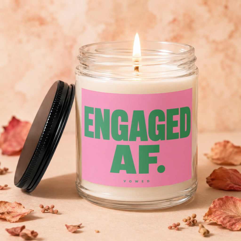 Candle with lit wick and pink label reading "ENGAGED AF. VOWED".