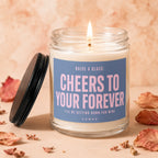 Glass candle with lit wick and label saying "Cheers to Your Forever Vowed".