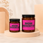 Two MOH Emergency Kit candles with pink labels, listed as safety pins, snacks, this candle.