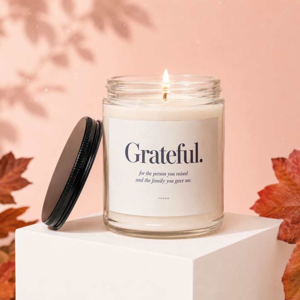 Candle with "Grateful" text on label, lit flame, black lid, and autumn leaves.
