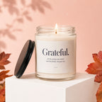Candle with "Grateful" text on label, lit flame, black lid, and autumn leaves.