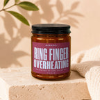 Amber jar candle with label saying "Ring Finger Overheating" and "She Said Yes."