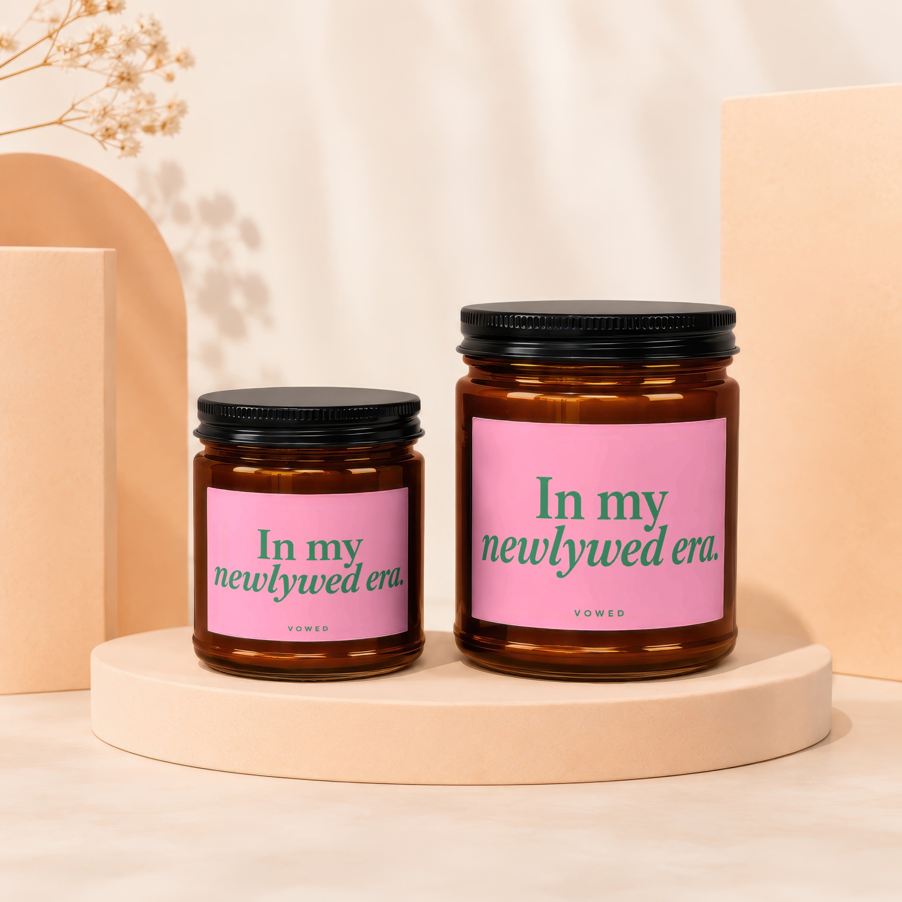 Two amber glass candles with pink labels reading "In my newlywed era."