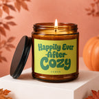 Amber candle with a lit wick and green label saying "Happily Ever After Cozy VOWED".