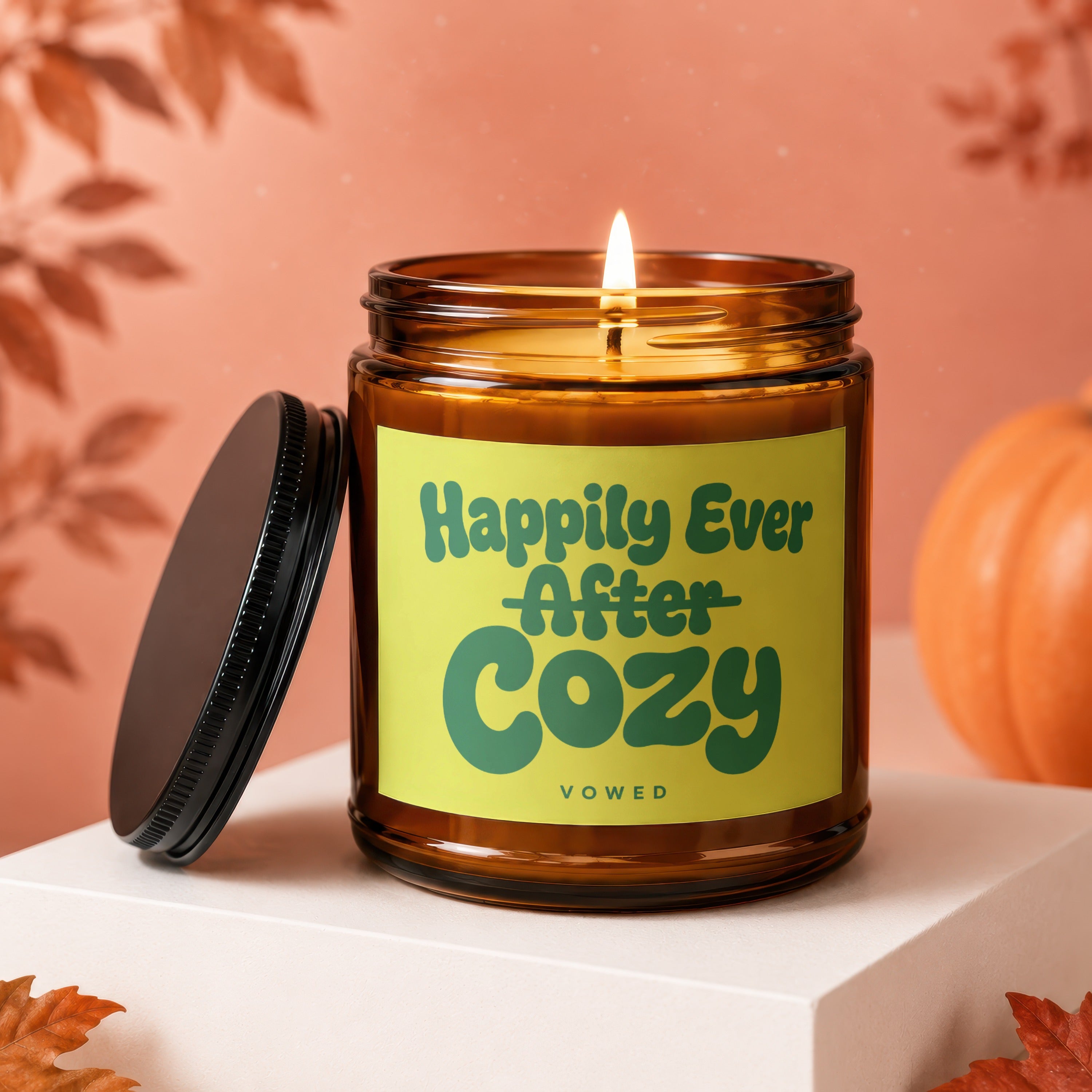 Amber candle with a lit wick and green label saying "Happily Ever After Cozy VOWED".