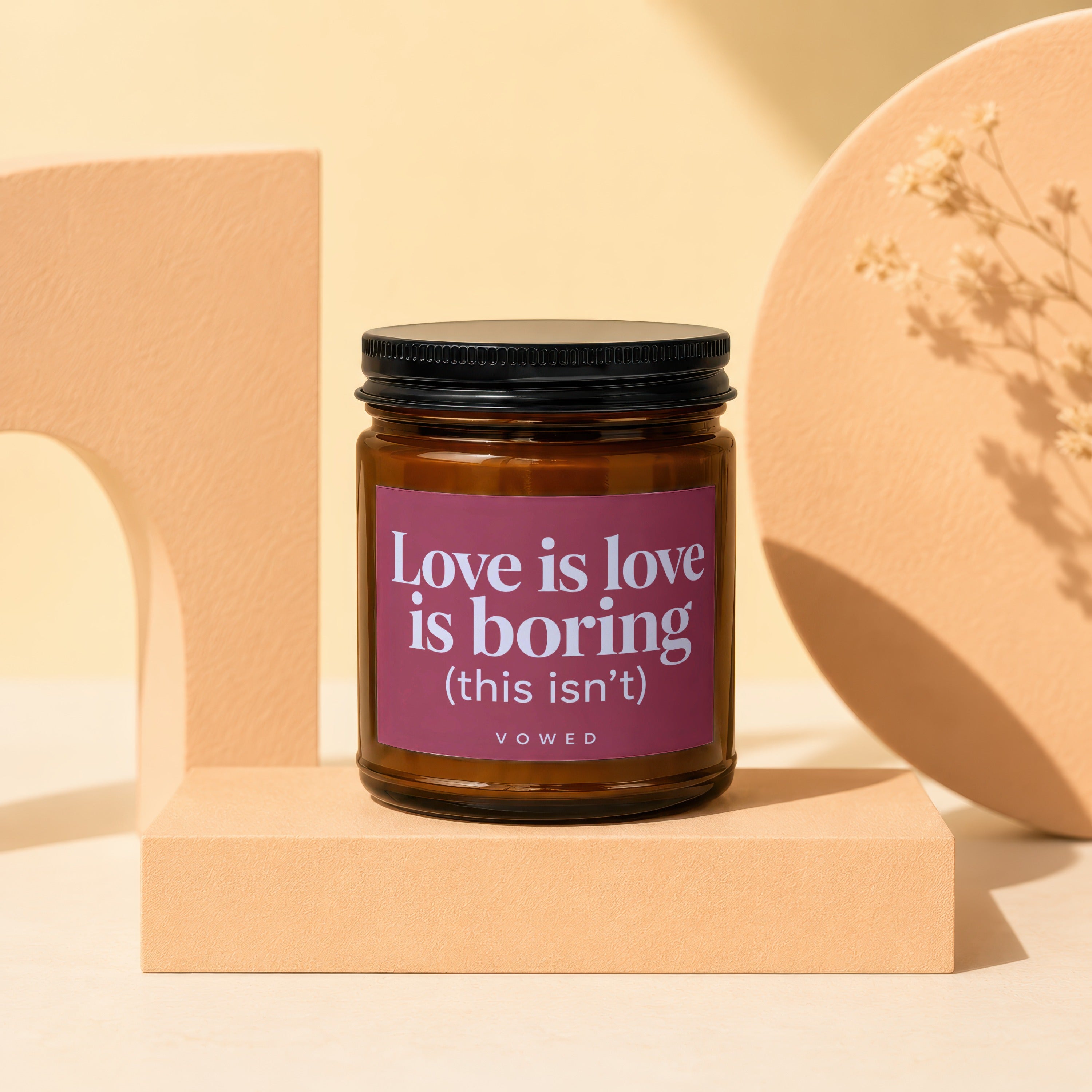 Amber-colored jar candle with a purple label saying "Love is love is boring (this isn't)".