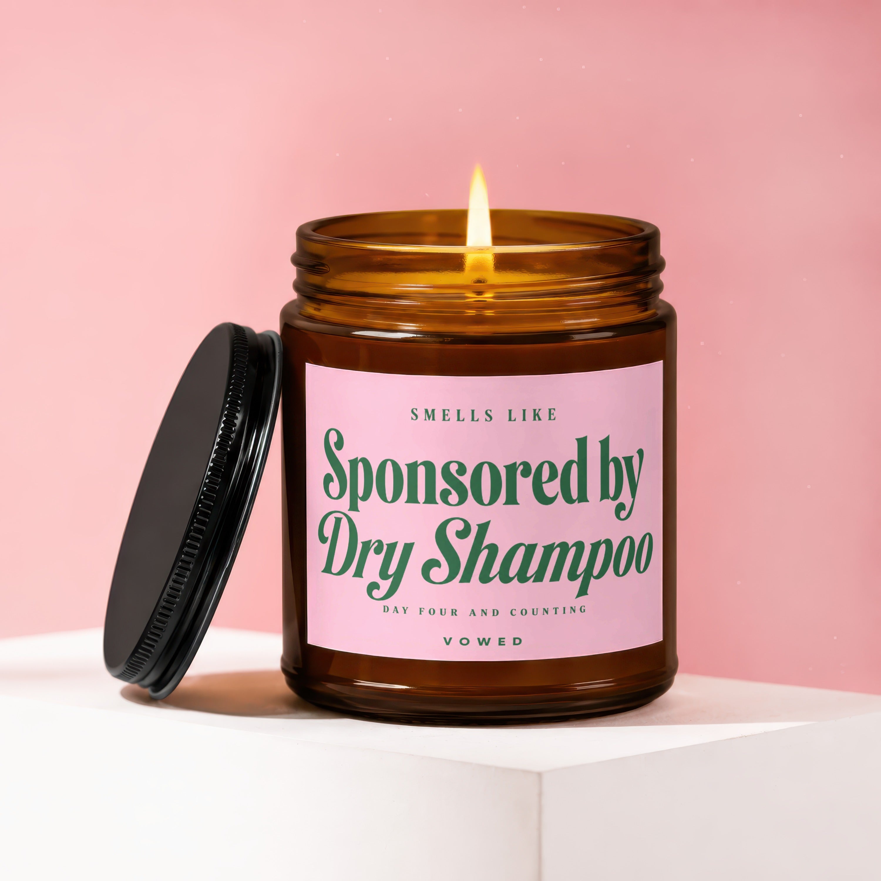 Amber jar candle with pink label says "Smells Like Sponsored by Dry Shampoo".