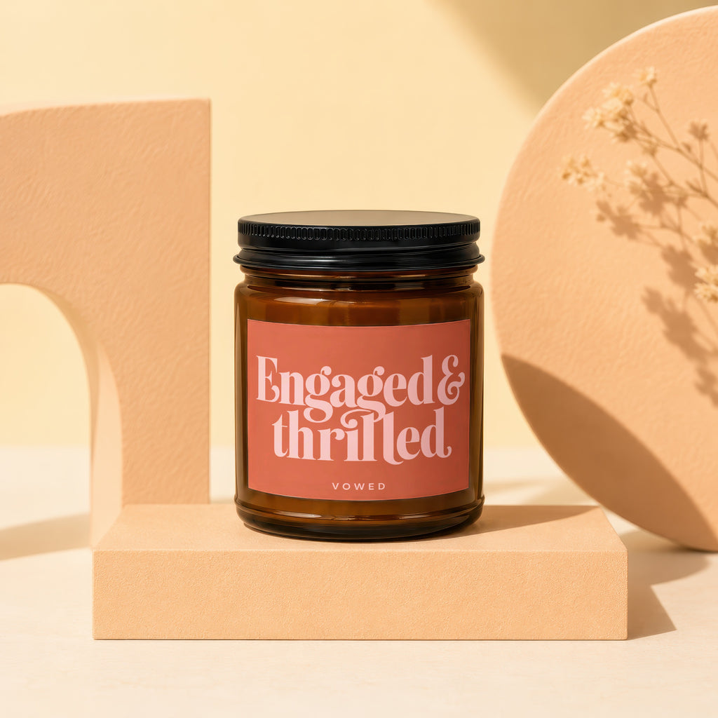 Candle with "Engaged & thrilled VOWED" text on label, amber jar, black lid.