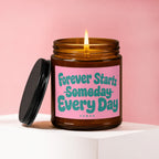 Amber candle burning with a pink label reading "Forever Starts Someday Every Day".