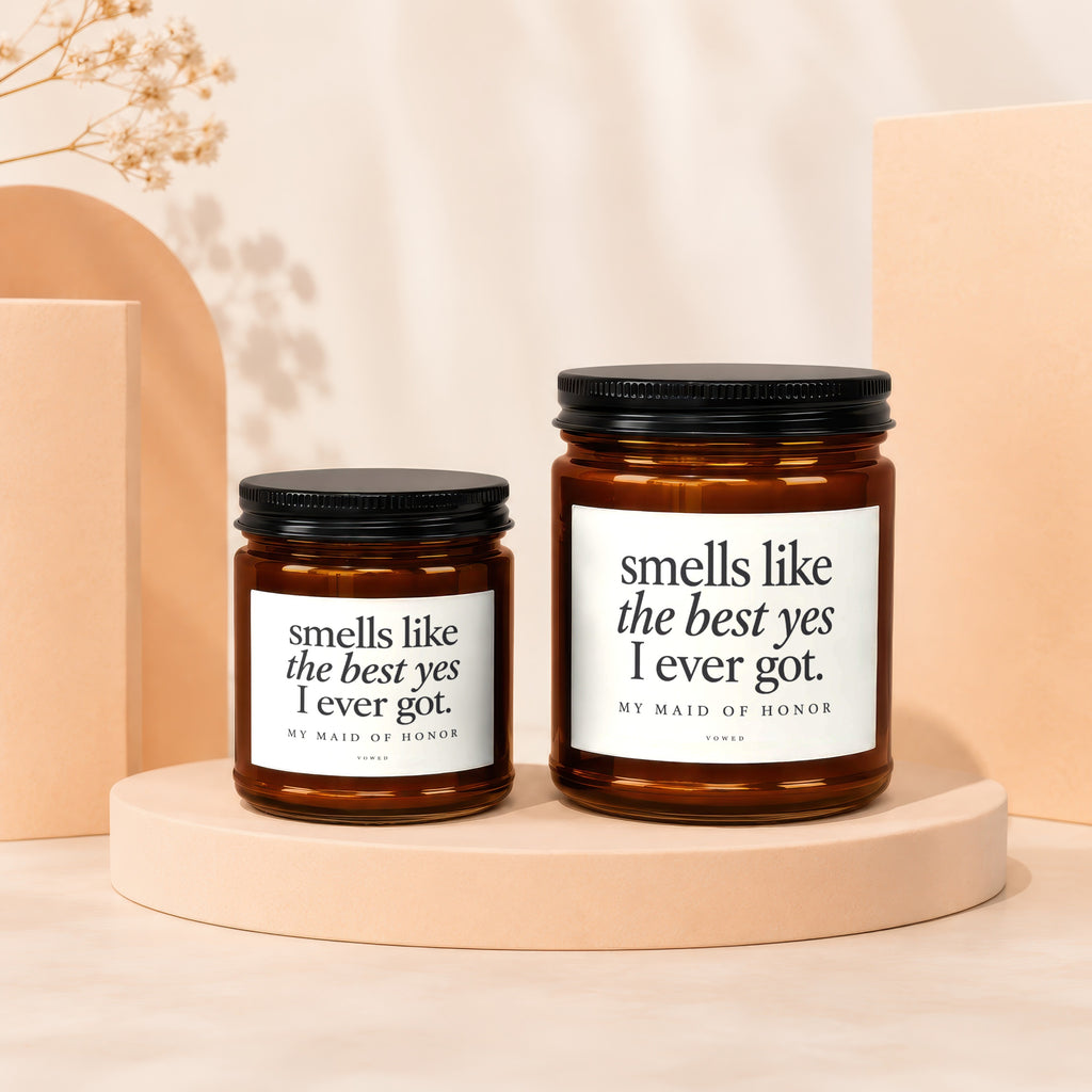 Two amber glass candles with black lids, labeled "smells like the best yes I ever got. MY MAID OF HONOR".