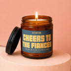 Amber candle with lit flame, black lid, and label reading "Cheers to the Fiances".