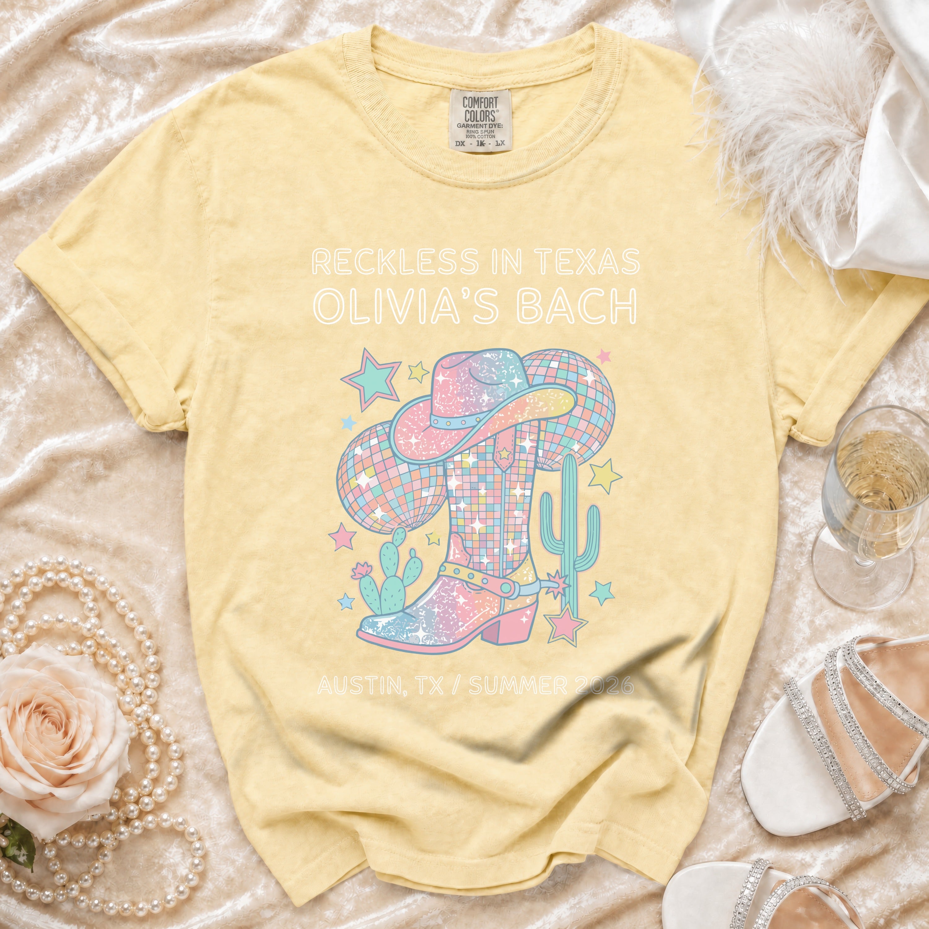 Yellow t-shirt with "Reckless in Texas Olivia's Bach" and pastel cowboy boot graphic.