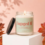 Glass candle with "Engaged AF" text, lid off, surrounded by leaves.