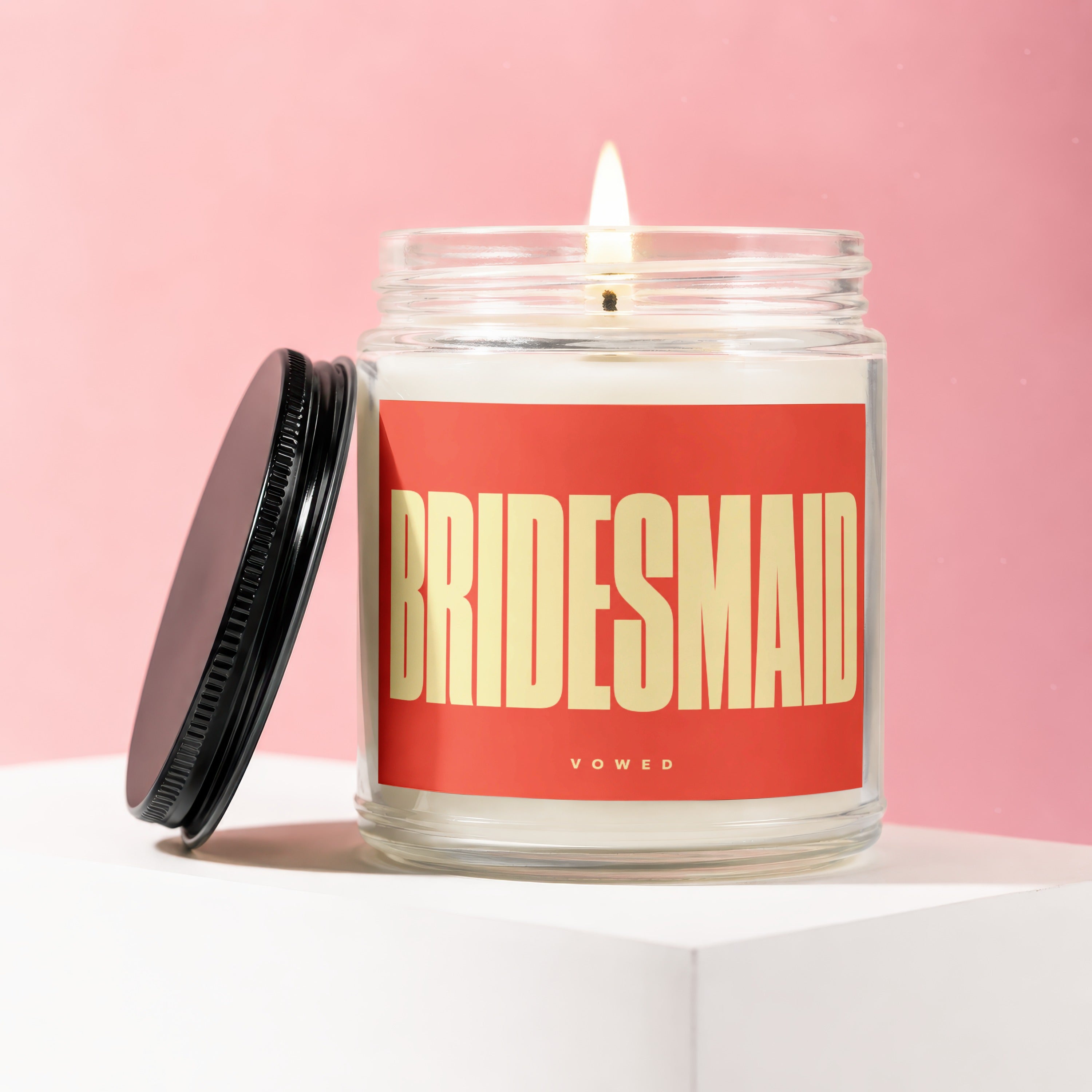 Bridesmaid candle in a glass jar with a lit wick and red label.