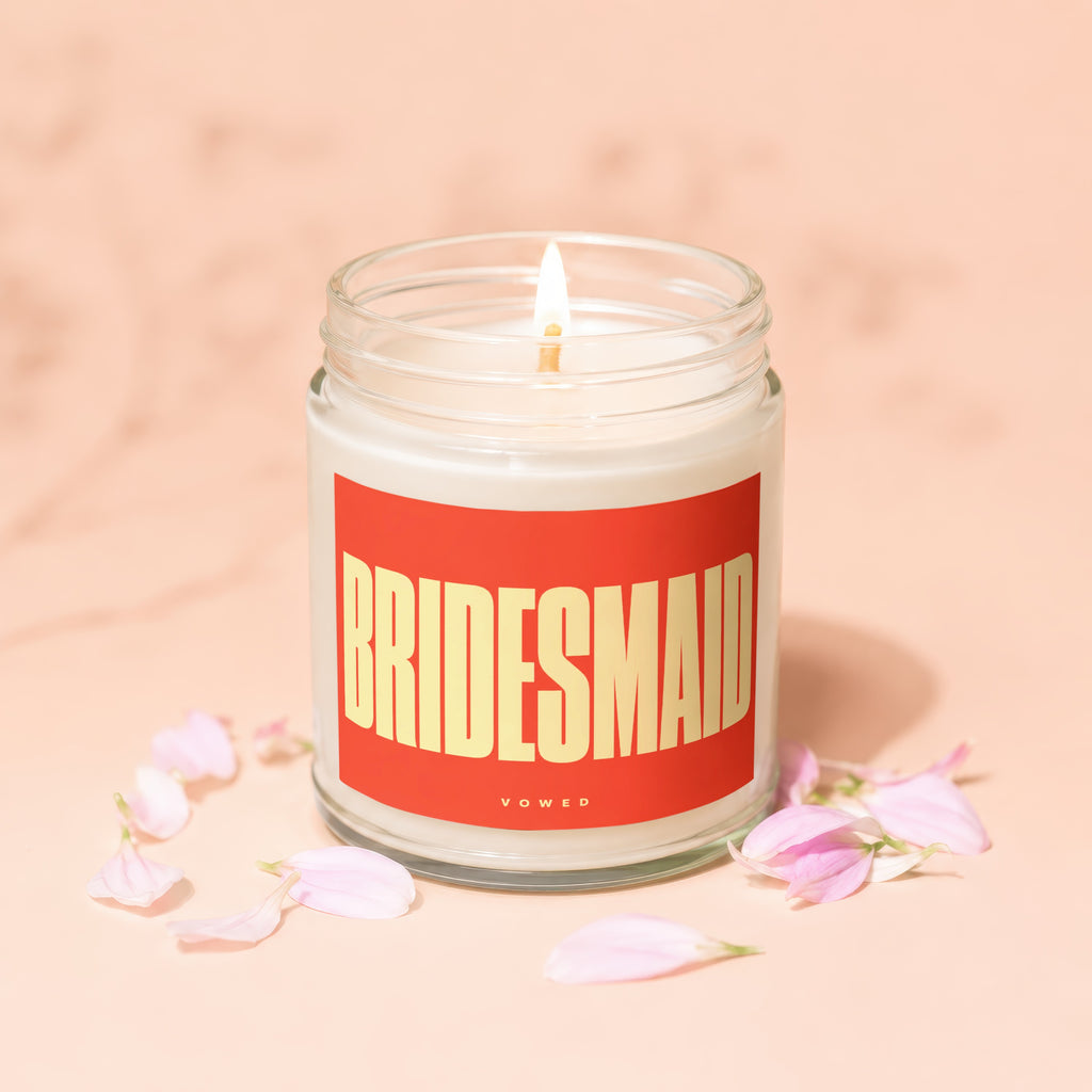 Candle labeled "BRIDESMAID" with the word "vowed" below, surrounded by pink flower petals.