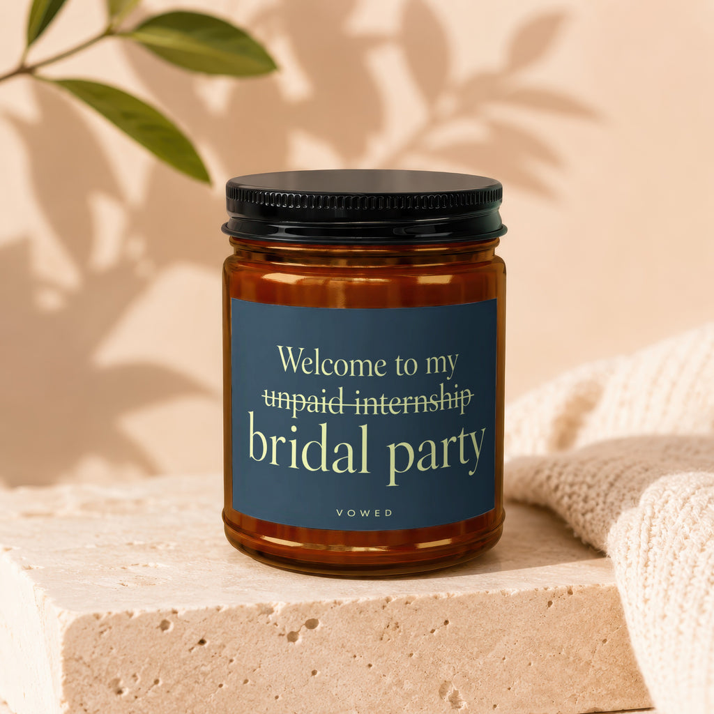 Amber jar candle with dark blue label reading "Welcome to my unpaid internship bridal party"