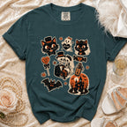 Teal t-shirt with Halloween-themed graphic featuring cats, skeletons, and a haunted house.