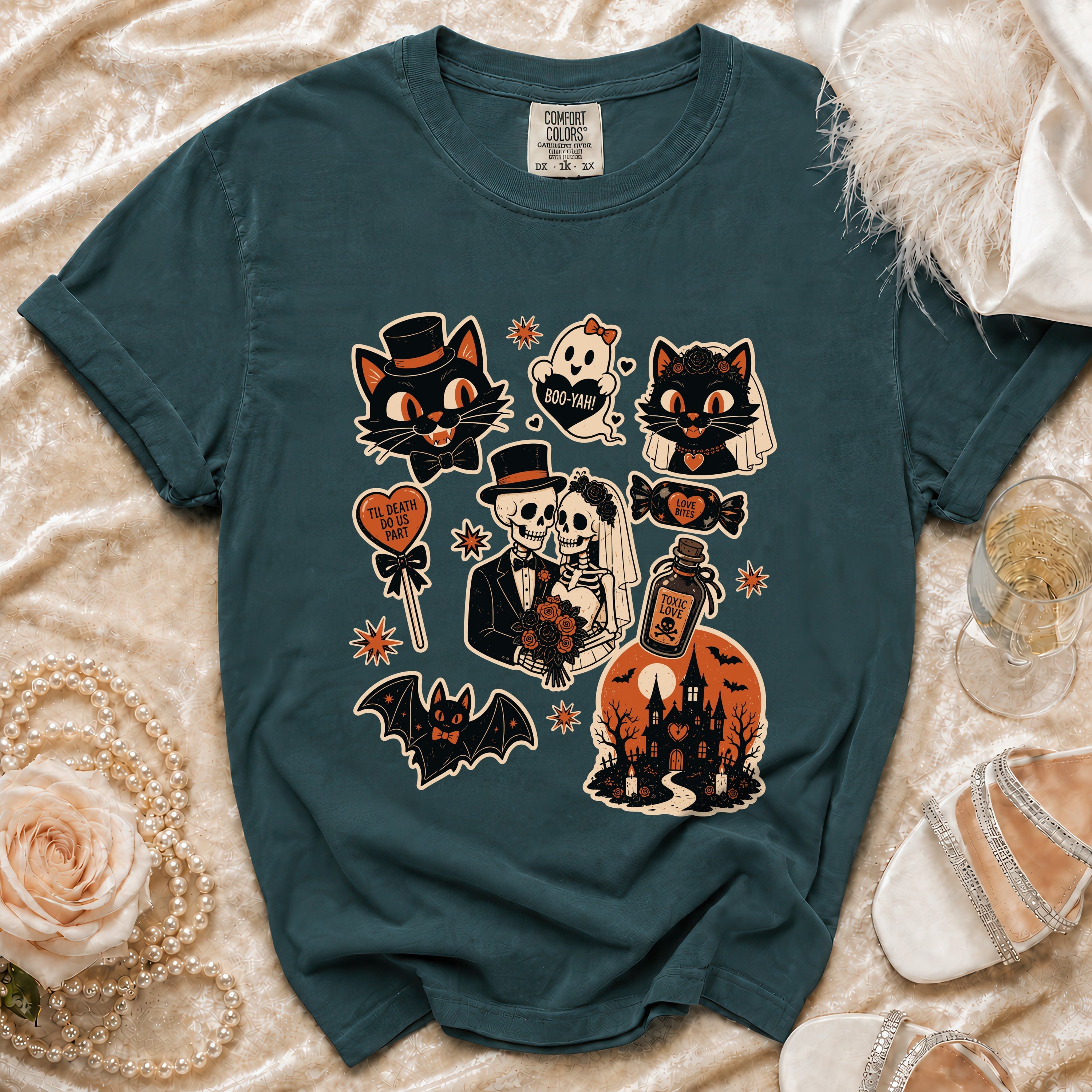 Teal t-shirt with Halloween-themed graphic featuring cats, skeletons, and a haunted house.