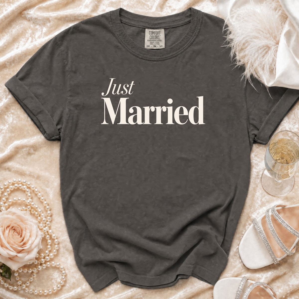 Dark grey t-shirt with "Just Married" text, styled with pearls, a rose, and champagne.