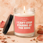 Candle with lit wick and pink label that reads "I can't stop staring at the ring."