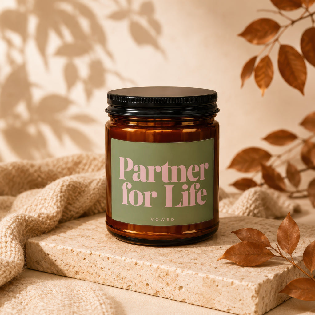 Amber jar candle with "Partner for Life" text on a green label, on a textured block.