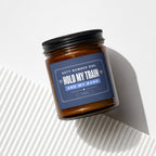 Brown glass candle with "Hold My Train And My Hand" text on a navy label.