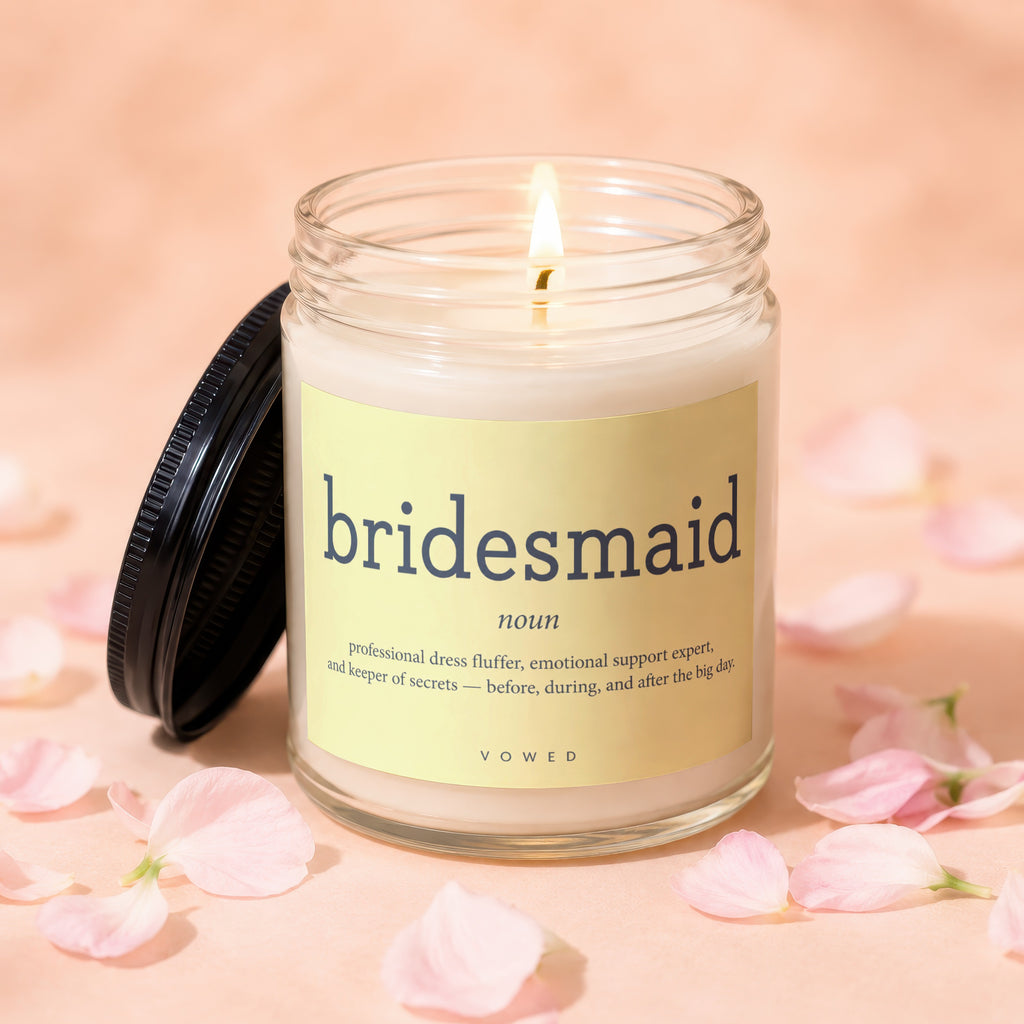 A lit bridesmaid-themed candle with a definition label surrounded by pink petals.