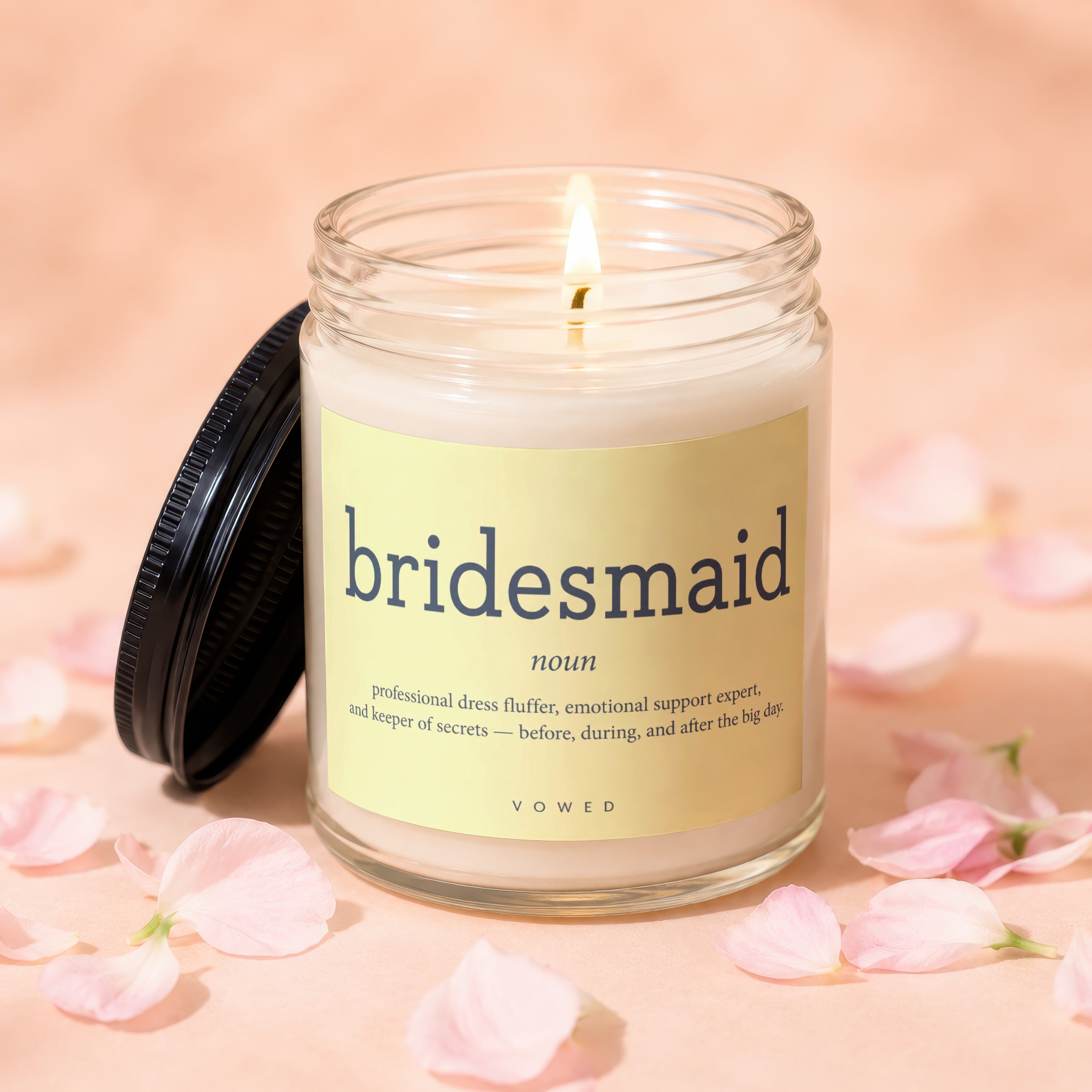 A lit bridesmaid-themed candle with a definition label surrounded by pink petals.