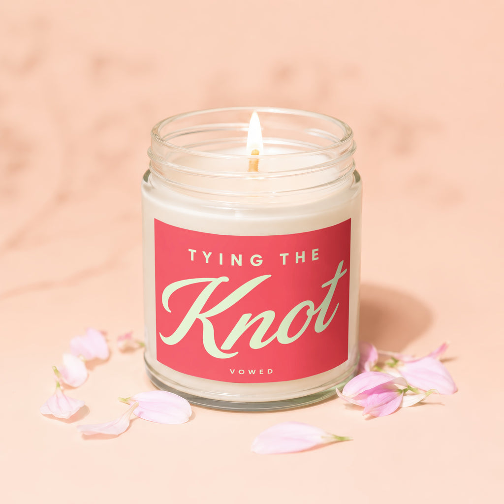 Lit candle in a glass jar with "TYING THE Knot" text and pink petals.