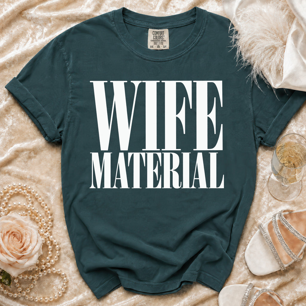 Teal t-shirt with white text "WIFE MATERIAL", styled with pearls and shoes.