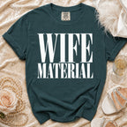 Teal t-shirt with white text "WIFE MATERIAL", styled with pearls and shoes.