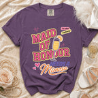 Purplish t-shirt with "Maid of Honour Needs a Mimosa" text and celebratory graphics.