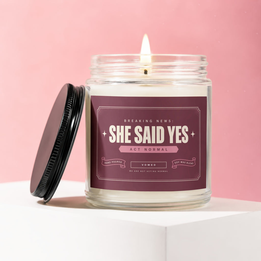 Lit candle in glass jar with "SHE SAID YES" label, lid off.
