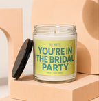 Candle with black lid and yellow label reading "YOU'RE IN THE BRIDAL PARTY".
