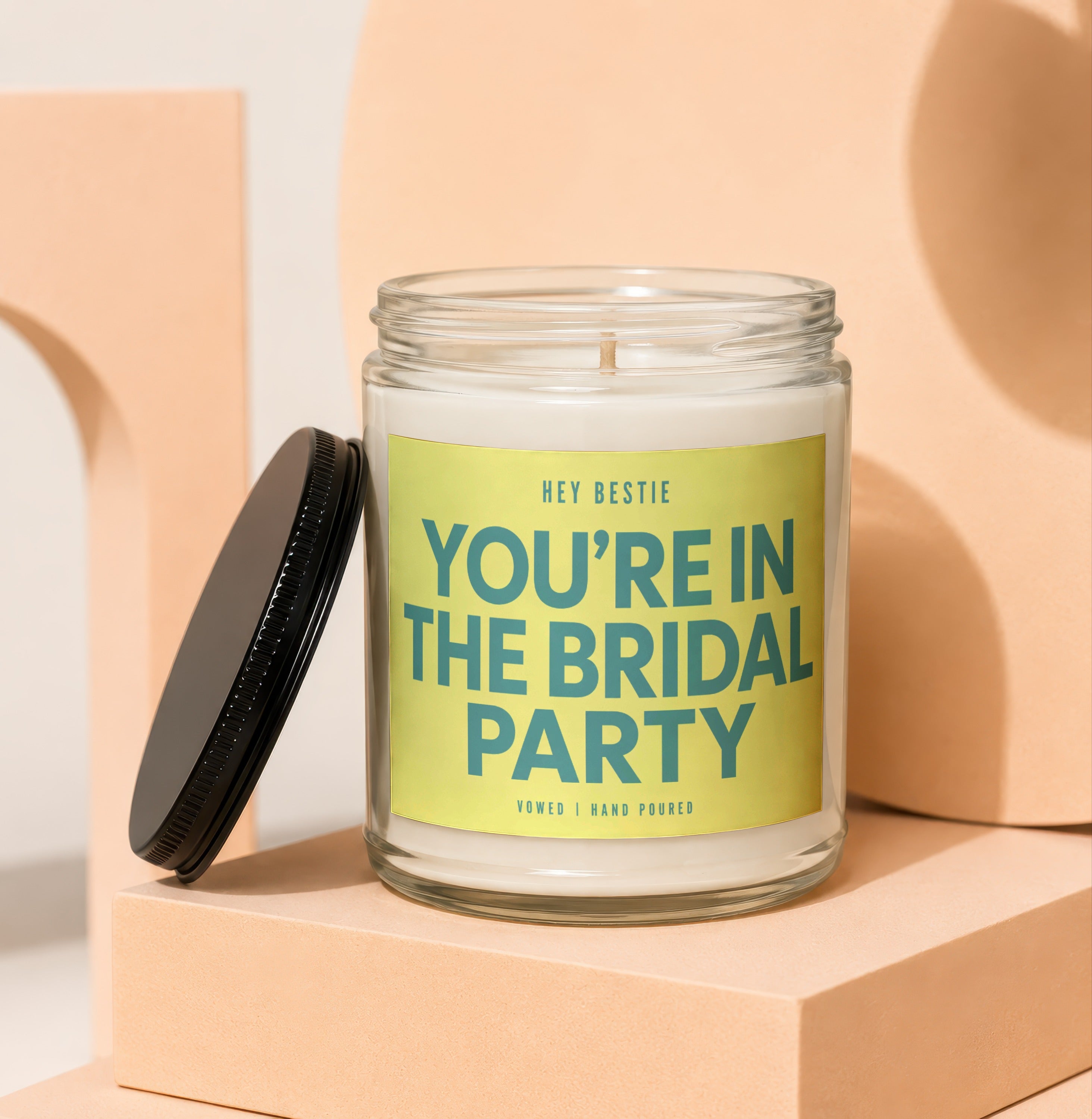 Candle with black lid and yellow label reading "YOU'RE IN THE BRIDAL PARTY".