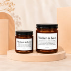 Two amber glass candles with black lids, labeled "Mother-in-Love."