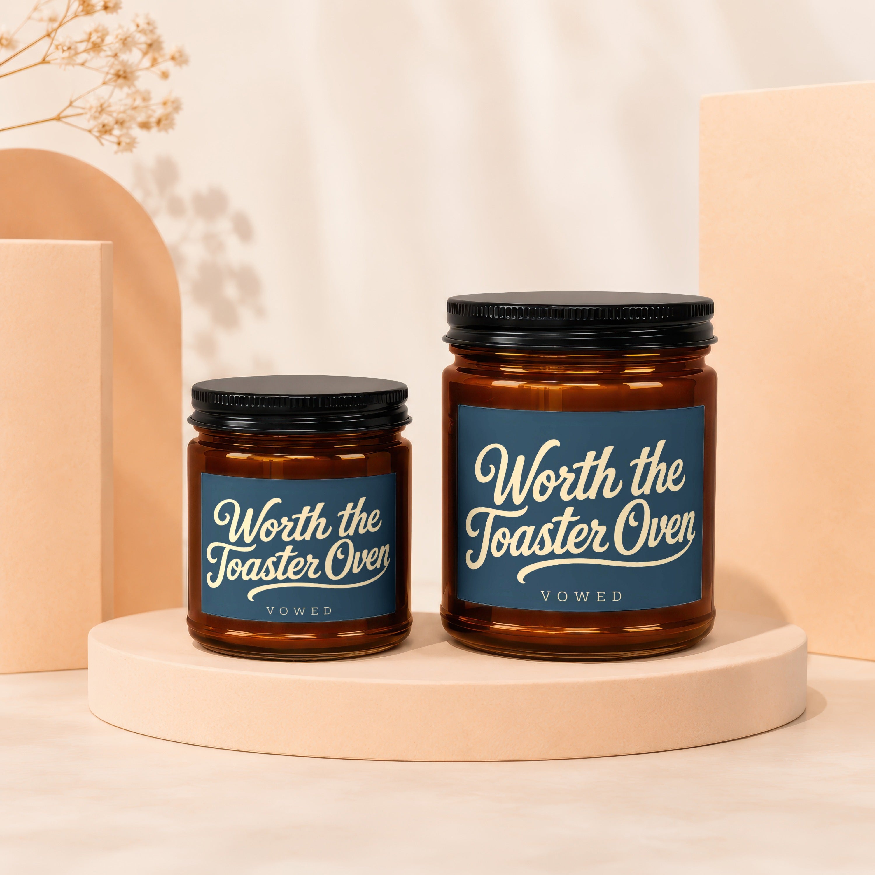 Two amber glass candles with black lids, blue labels reading "Worth the Toaster Oven."