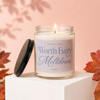Candle with "Worth Every Meltdown" text on a white pedestal with fall leaves.
