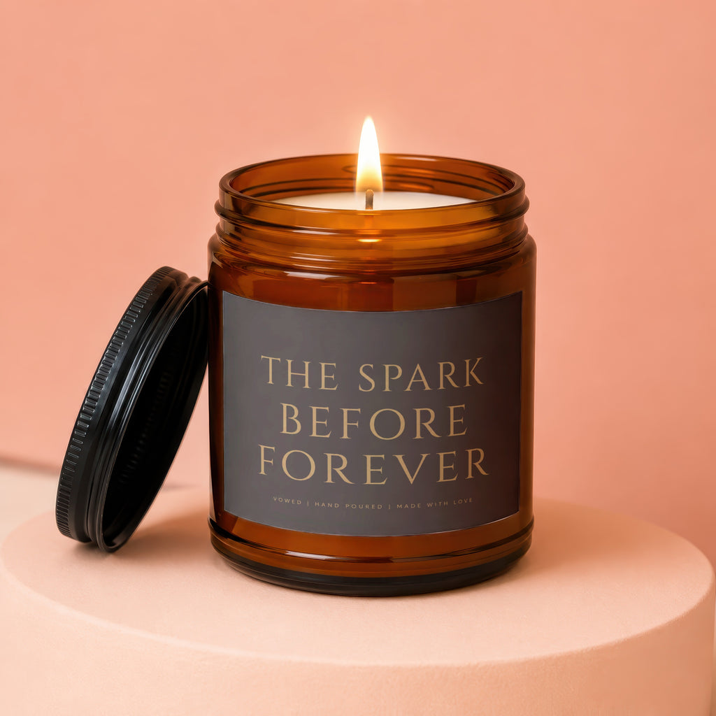 Lit amber glass candle with label reading "The Spark Before Forever".