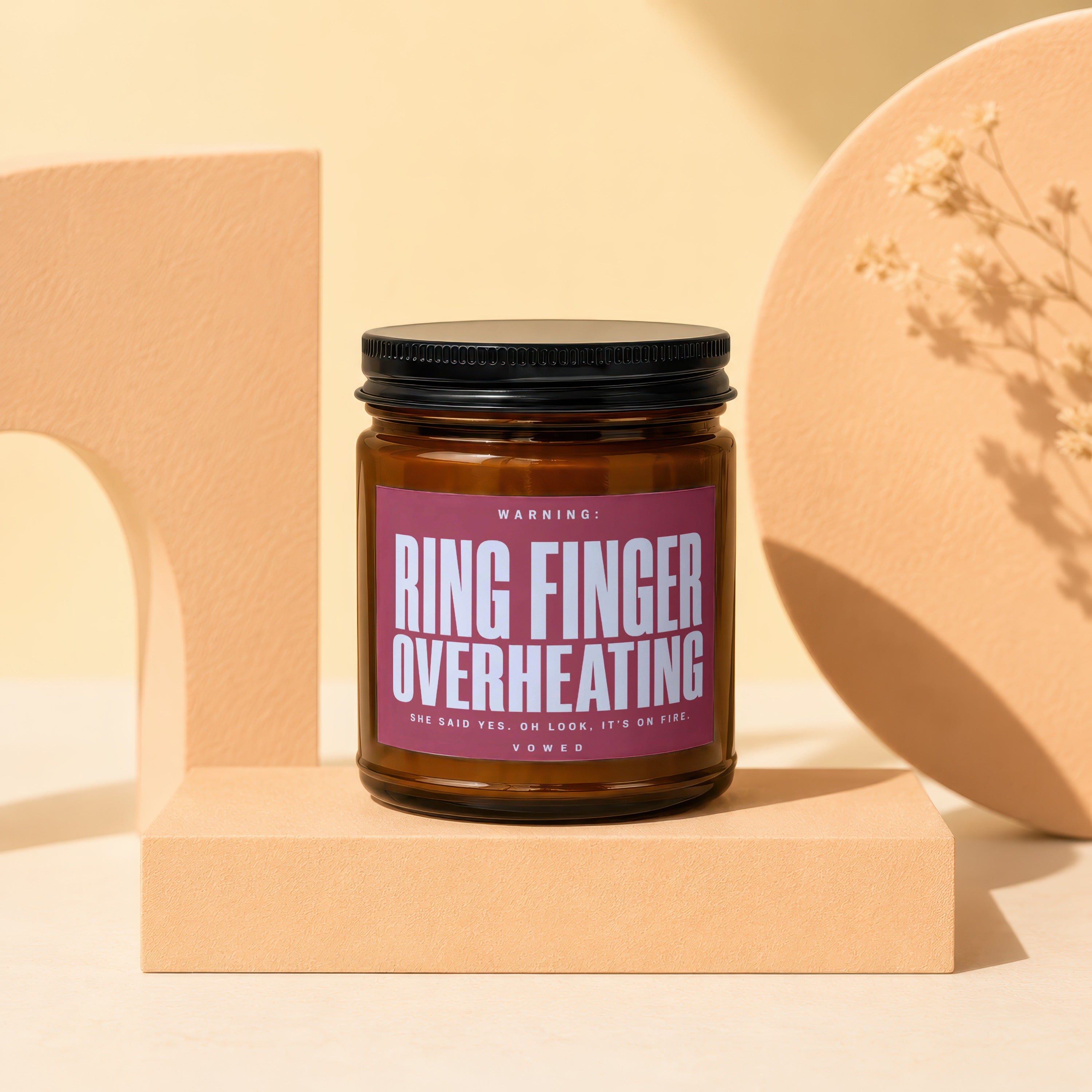 Amber candle with "Ring Finger Overheating" label on a cream platform.