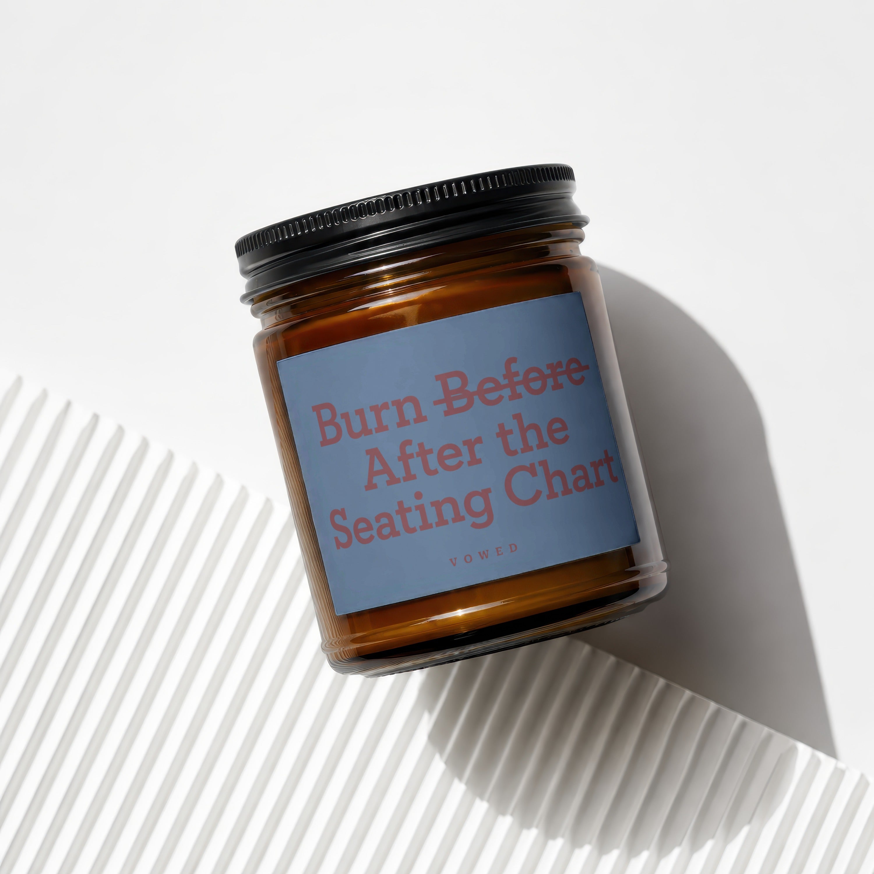 Candle with black lid and blue label reading "Burn Before After the Seating Chart."
