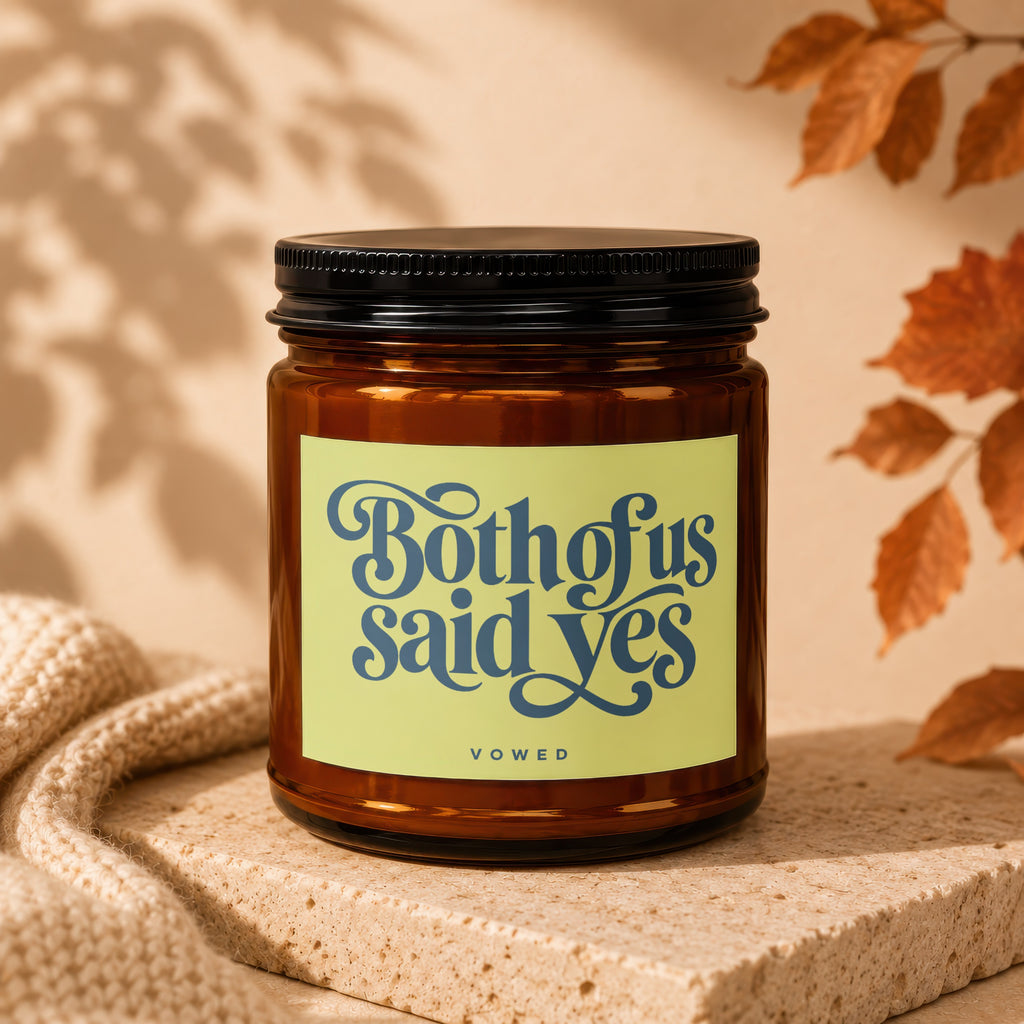Amber glass candle with a pale yellow label that reads "Both of us said yes" above "vowed".