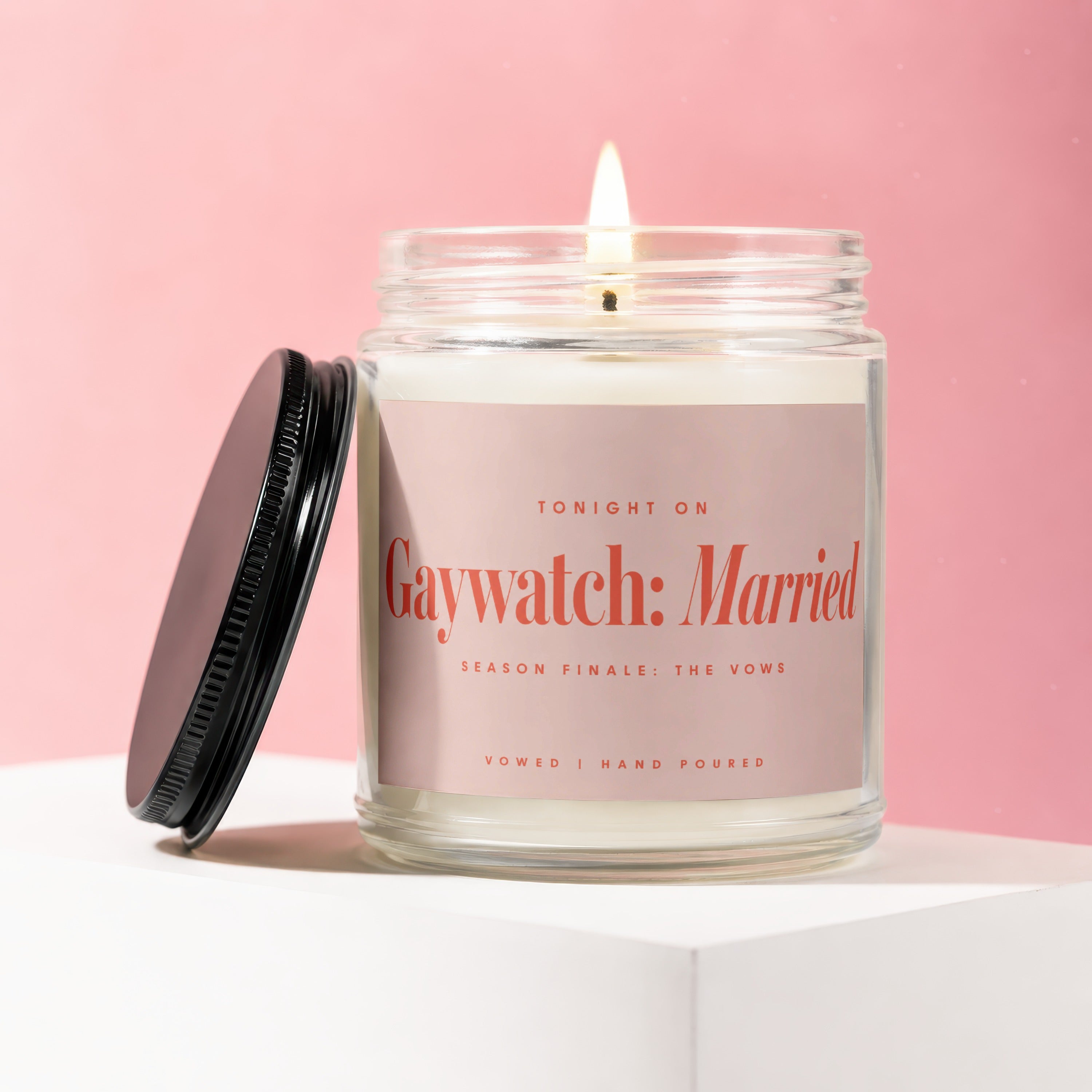Glass candle with lit wick, light pink label reading "Gaywatch: Married"