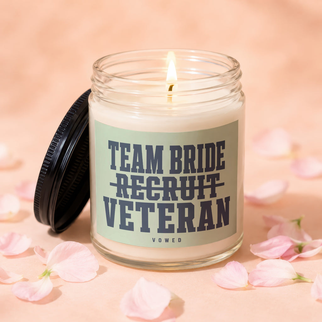 Candle with "Team Bride Recruit Veteran" text and a burning wick, surrounded by petals.