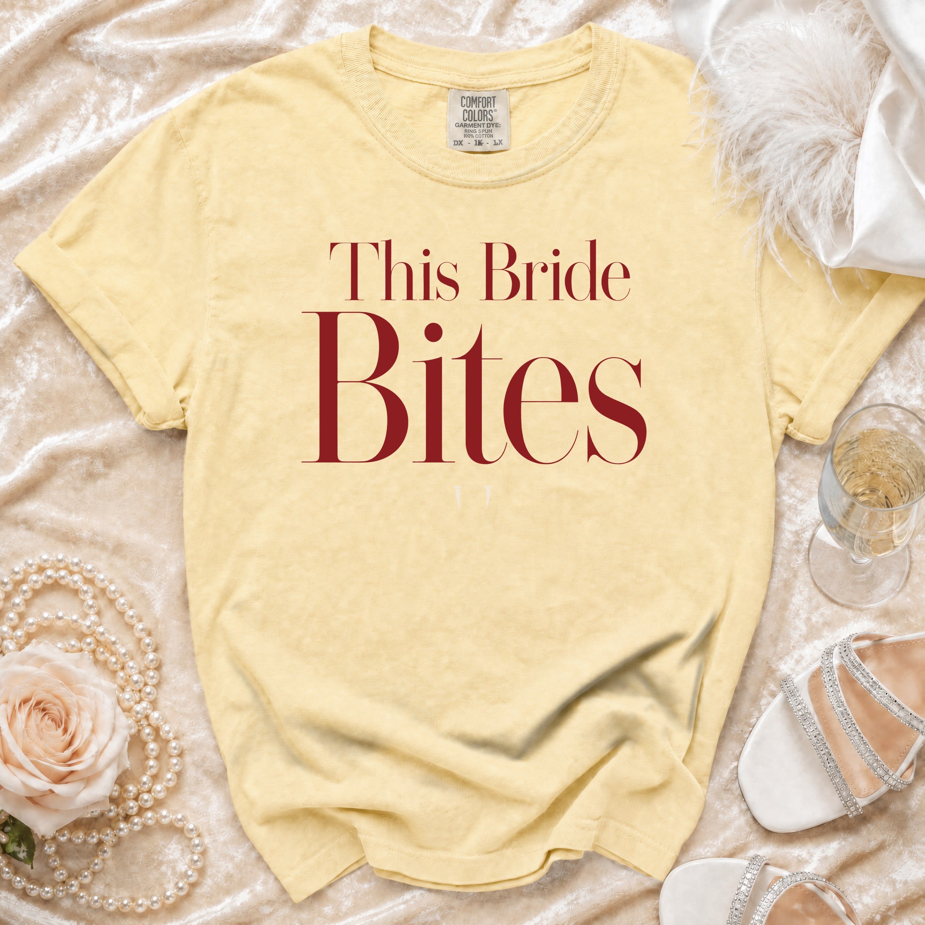 Yellow t-shirt with maroon text "This Bride Bites" and bridal accessories.