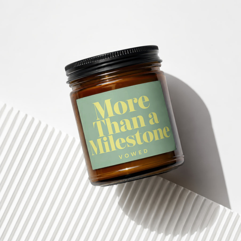 Amber glass candle with a green label reading "More Than a Milestone VOWED."