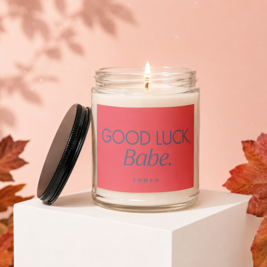 Lit candle in glass jar with pink label reading "GOOD LUCK, Babe. VOWED"