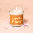 Burning candle with orange label reading "Everyday Love Vowed" surrounded by pink flower petals.