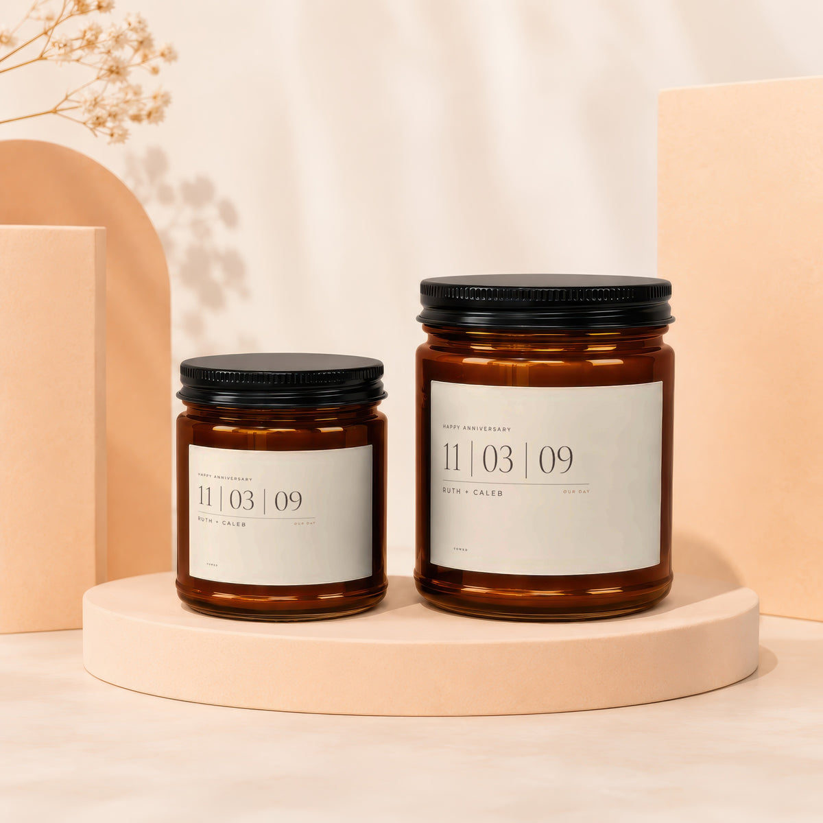 Two amber glass candles with black lids, labeled "Happy Anniversary 11 | 03 | 09 Ruth + Caleb Our Day".