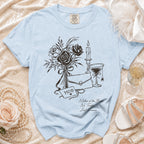 Light blue t-shirt with graphic of roses, candle, martini glass, and text "MOB Mother of the Bride No Tricks Just Trauma."